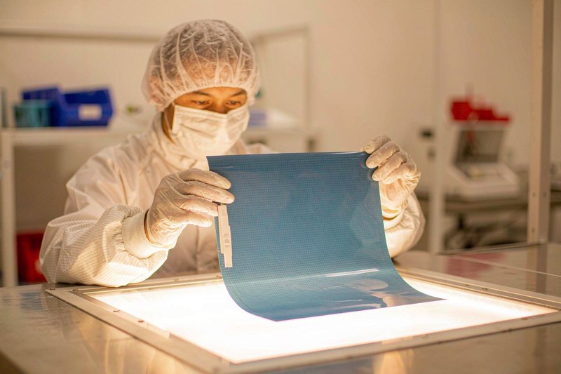 Operator inspecting a blue opaque PET release film sheet on a light panel in a cleanroom